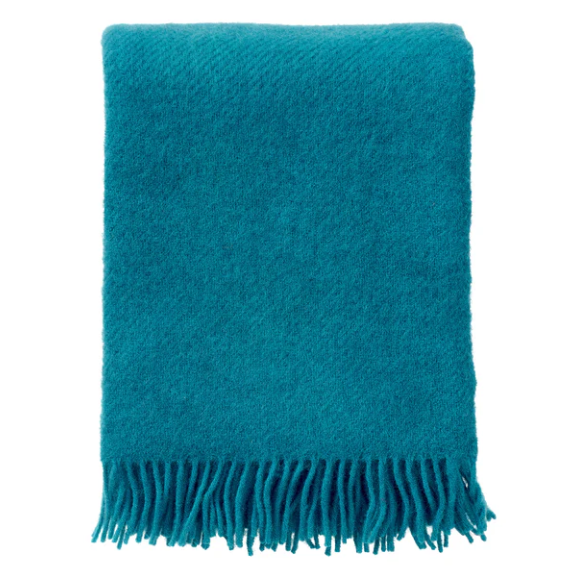 Teal blanket with fringes on a white background, displayed on a website for Klippan.